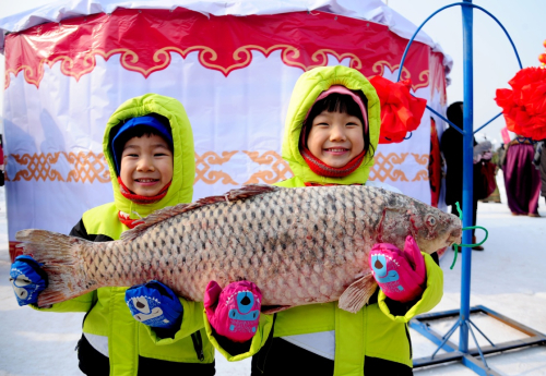 1月16日，兩個(gè)孩子手捧冬捕節(jié)上打撈的魚合影留念。當(dāng)日，為期一個(gè)半月的第四屆遼寧康平臥龍湖大遼文化冬捕節(jié)在沈陽(yáng)市康平縣臥龍湖開幕，期間舉行遼代祭祖儀式、祭湖醒網(wǎng)儀式、觀看北方傳統(tǒng)古法捕魚、品嘗魚頭湯、看雪雕、逛廟會(huì)等豐富多彩的系列活動(dòng)。臥龍湖位于沈陽(yáng)北部，面積127.5平方公里，是遼寧省最大的平原淡水湖。當(dāng)?shù)氐拇筮|文化冬捕節(jié)已經(jīng)連續(xù)舉辦三屆，遼代元素貫穿整個(gè)冬捕活動(dòng)，成為遼寧北部地區(qū)獨(dú)具特色的冬季旅游品牌。新華社發(fā)（張文魁 攝）